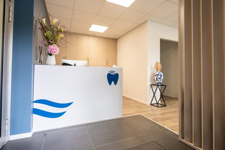 Réception du Centre Dentaire Porte de Versoix, l’emblème bleu en forme de dent sur le comptoir.